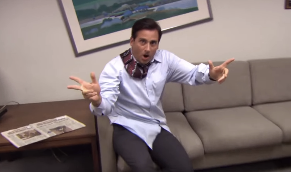 Man in office making finger guns, wearing white shirt and tie; comedic expression