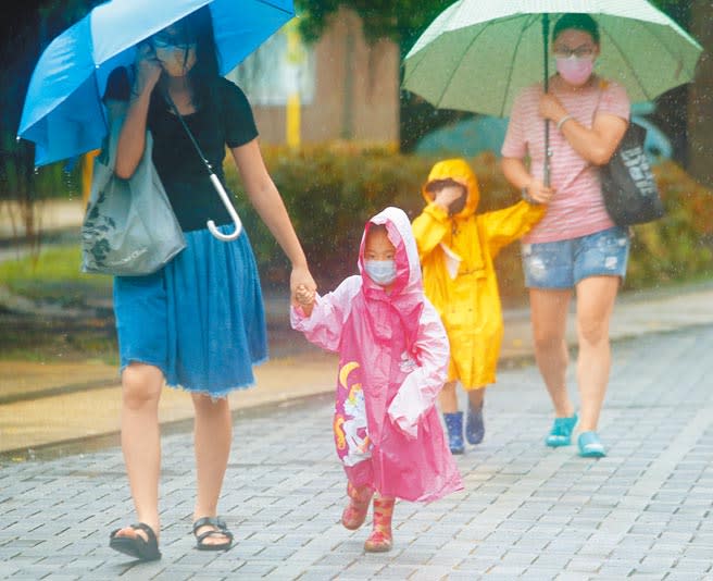 受中颱璨樹影響，北台灣12日下午風雨才逐漸加大。圖為家長帶著穿雨衣的小朋友在淡水街頭冒雨趕路。（陳君瑋攝）