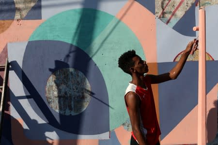 A community member helps to artist Fabian Solymar to paint a mural in a wall at the slum of Petare, in Caracas