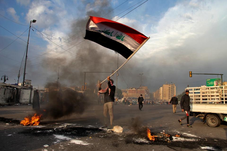 A protester waves the national flag while demonstrators set fire to close streets near Tahrir Square in Baghdad, Iraq, on Jan. 8, 2020.