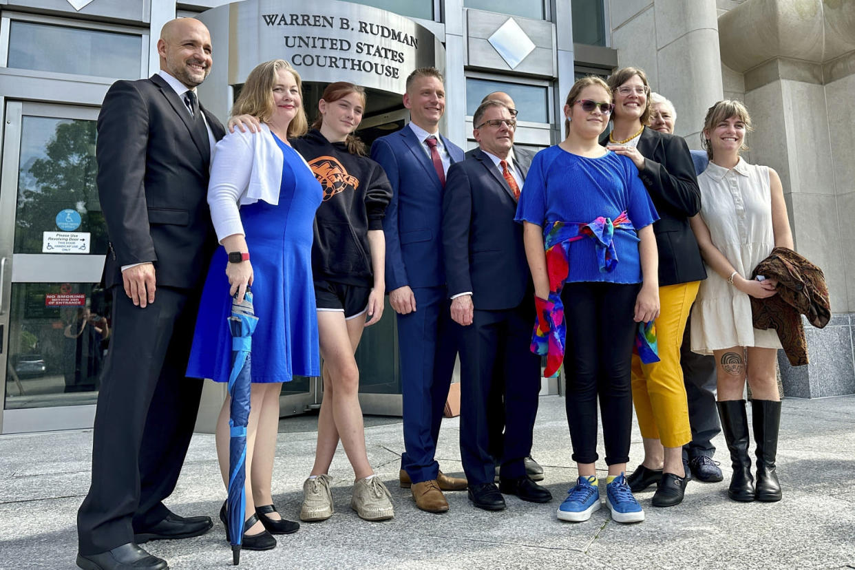 Two teens challenging New Hampshire's new law banning transgender girls from girls' sports teams, Parker Tirrell, third from left, and Iris Turmelle, sixth from left, pose with their families and attorneys in Concord, N.H., Monday, Aug. 19, 2024. (Holly Ramer / AP)