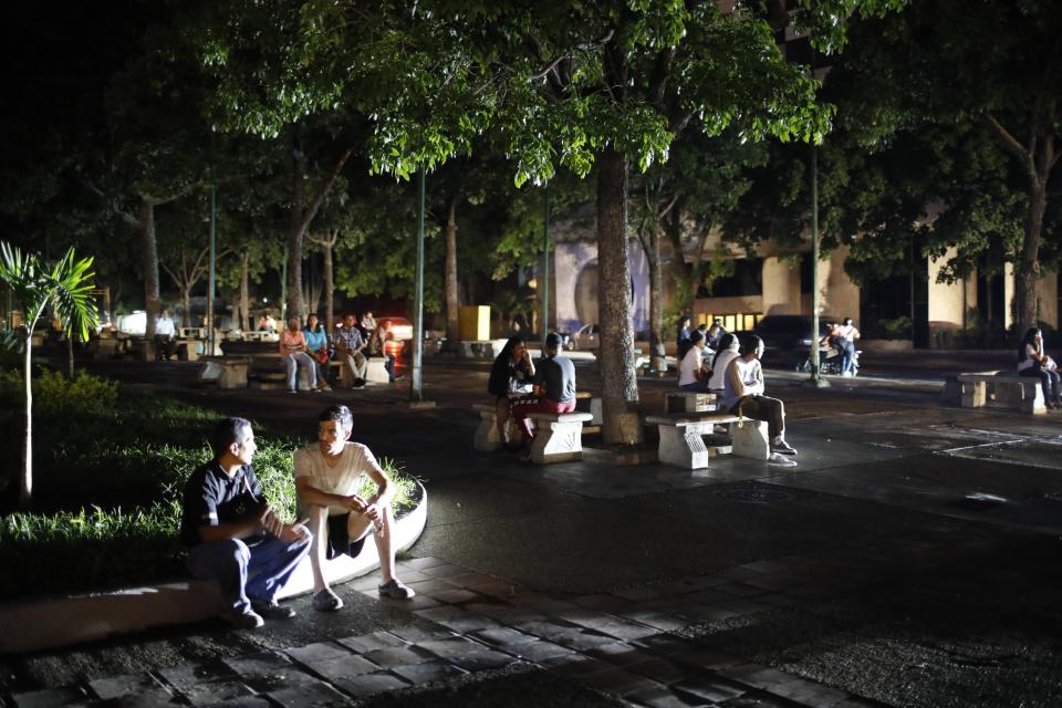 People seat on a square during a blackout in Caracas, Venezuela, Monday, July 22, 2019. The lights went out across much of Venezuela Monday, reviving fears of the blackouts that plunged the country into chaos a few months ago as the government once again accused opponents of sabotaging the nation's hydroelectric power system. (AP Photo/Ariana Cubillos)