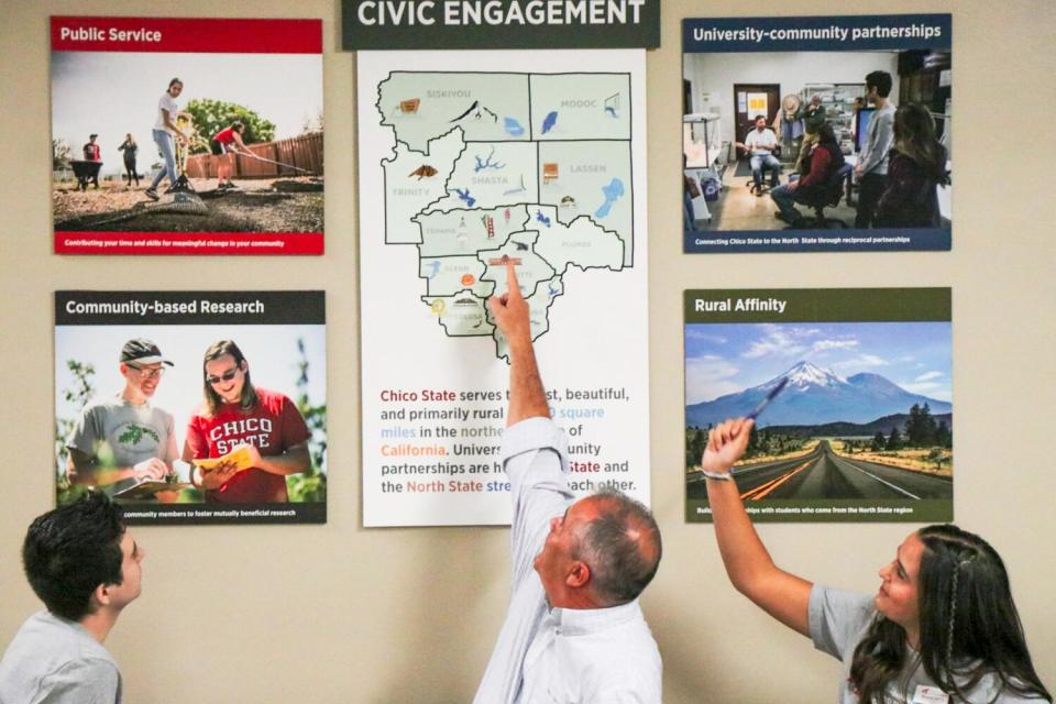 Two Cal State Chico students, left and right, look at a map with the university's president, Stephen Perez