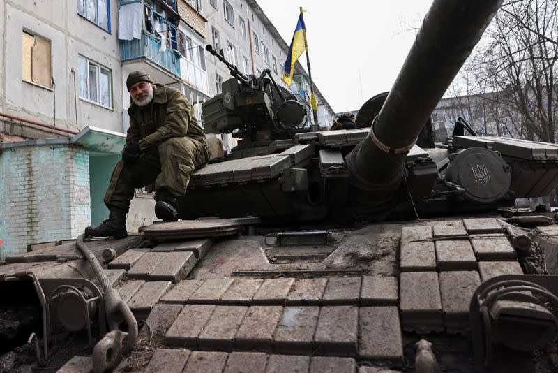 An Ukrainian serviceman sits atop a tank, near the bombed-out eastern city of Bakhmut