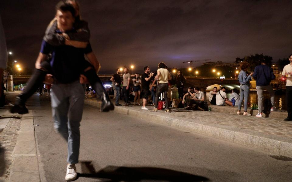 People stand on the banks of the Seine River past the 11pm Covid-19 curfew, early on June 12, 2021, after people gathered nearby at Les Invalides for an unauthorized outdoor party. - Geoffroy Van Der Hasselt/AFP