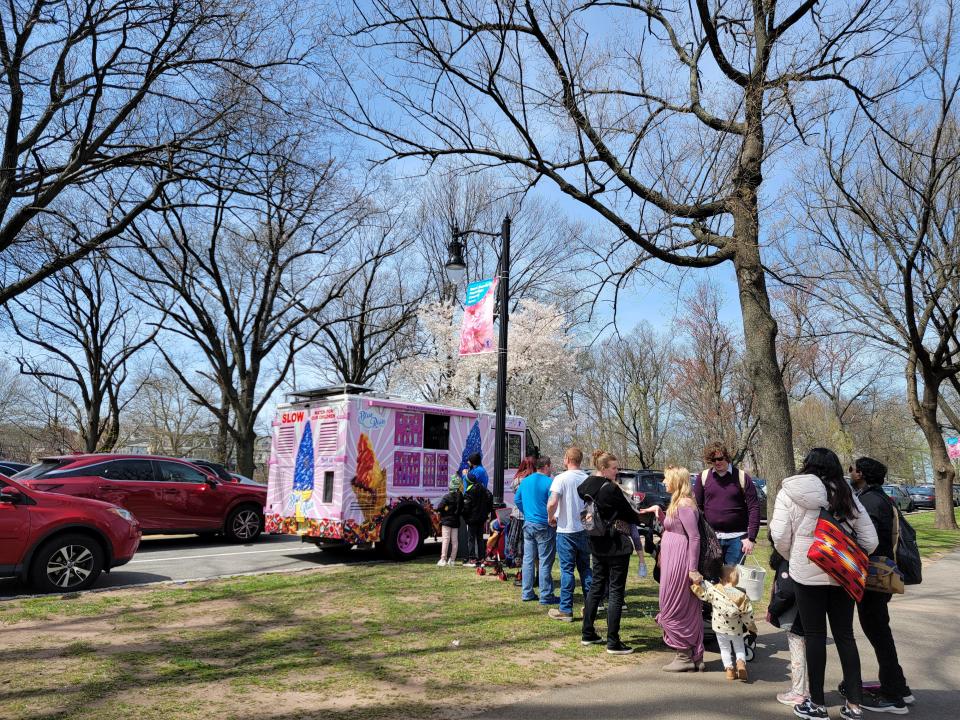 A dozen visitors including children line up at a pink truck decorated with ice cream cones.