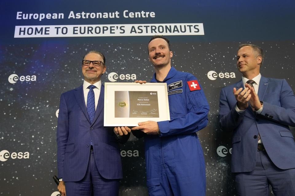 ESA director Josef Aschbacher, left, stands with Marco Sieber of Switzerland, center, at the candidates of the Class of 2022 graduation ceremony at the European Astronaut Centre in Cologne, Germany, Monday, April 22, 2024. ESA astronaut candidates Sophie Adenot of France, Pablo Alvarez Fernandez of Spain, Rosemary Coogan of Britain, Raphael Liegeois of Belgium and Marco Sieber of Switzerland took up duty at the European Astronaut Centre one year ago to be trained to the highest level of standards as specified by the International Space Station partners. Also concluding a year of astronaut basic training is Australian astronaut candidate Katherine Bennell-Pegg, who has trained alongside ESA's candidates. (AP Photo/Martin Meissner)