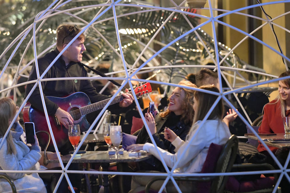 An entertainer plays for people sitting in restaurants in the old part of Bucharest, Romania, Friday, Oct. 23, 2020. In much of Europe, city squares and streets, be they wide, elegant boulevards like in Paris or cobblestoned alleys in Rome, serve as animated evening extensions of drawing rooms and living rooms. As Coronavirus restrictions once again put limitations on how we live and socialize, AP photographers across Europe delivered a snapshot of how Friday evening, the gateway to the weekend, looks and feels. (AP Photo/Andreea Alexandru)