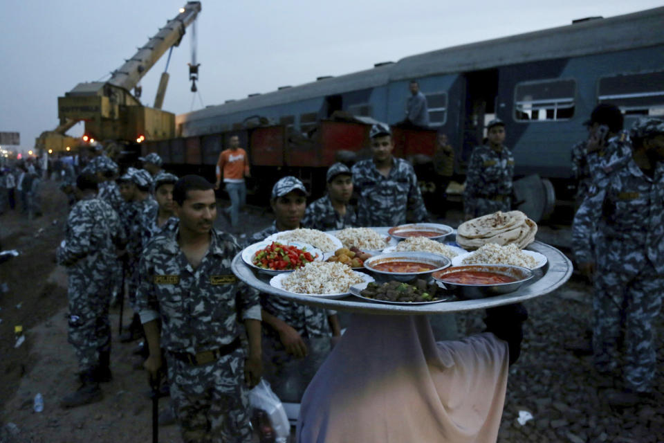 A woman brings food for security forces to break their fast during the holy month of Ramadan, at the site of a passenger train that derailed injuring around 100 people, near Banha, Qalyubia province, Egypt, Sunday, April 18, 2021. At least eight train wagons ran off the railway, the provincial governor's office said in a statement. (AP Photo/Fadel Dawood)