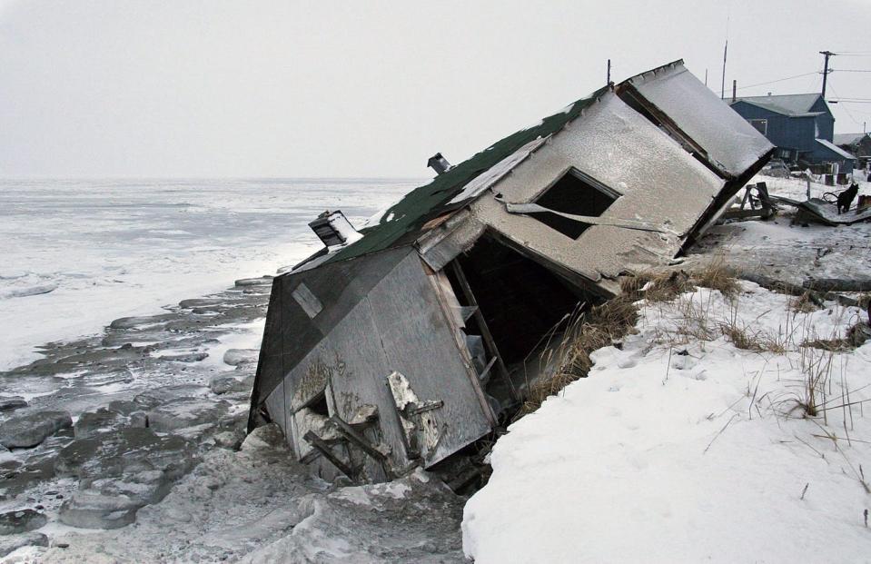 A single-storey house falling off a snow-covered shoreline into the ocean.