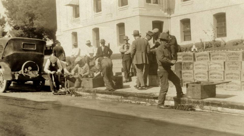 San Luis Obispo County Sheriff’s deputies dispose of illegal beer and Canadian whiskey in front of the courthouse, after a Prohibition raid circa 1921. Crates labeled Falstaff and Anheuser-Busch are on sidewalk as the gutter fills with suds.