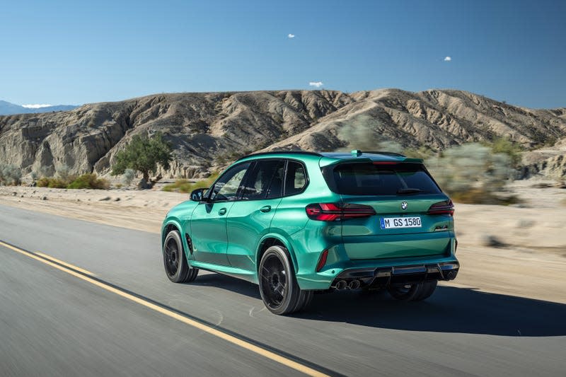 A green metallic 2024 BMW X5M Competition drives in the desert, rear three-quarter view