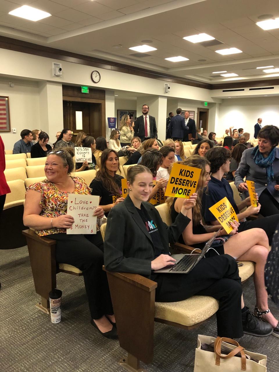 People hold signs before the start of a working group meeting to discuss Tennessee potentially rejecting nearly $2 billion in federal K-12 funding.