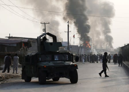 Policemen keep watch as angry Afghan protesters burn tires and shout slogans at the site of a blast in Kabul