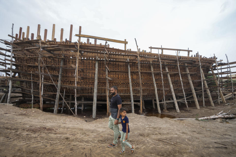 A man and a child walk past a vessel being made at Mandvi, a coastal town famous for boatmakers in Kutch district of Gujarat state, India, Wednesday, June 14, 2023. With Cyclone Biparjoy expected to make landfall Thursday evening, coastal regions of India and Pakistan are on high alert. (AP Photo/Ajit Solanki)