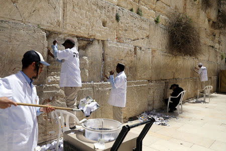 Men clear notes placed in the cracks of the Western Wall, Judaism's holiest prayer site, to create space for new notes ahead of the Jewish holiday of Passover, in Jerusalem's Old City, March 20, 2018. REUTERS/Ammar Awad