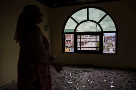 A woman stands next to a broken window of her house that was allegedly damaged by Indian security personnel after clashes between protesters and security forces during restrictions, in Srinagar