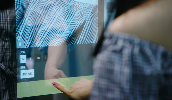 A woman uses a digital screen in a fitting room to request a new size