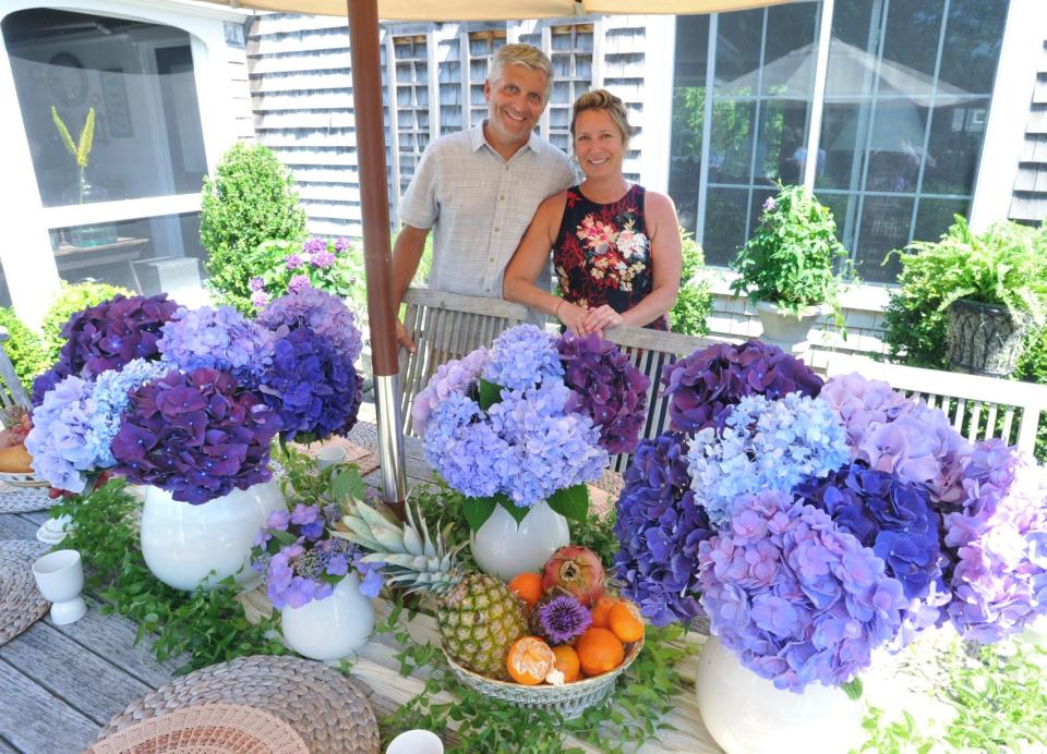 Chad and Bonnie Frost stand near a table decorated with hydrangea arrangements at their Duxbury home during the hydrangea garden tour hosted by the Community Garden Club of Duxbury, Tuesday, July 12, 2022.