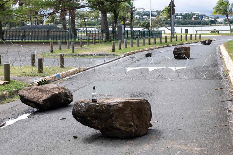 Alambre de espino y piedras bloquean la salida del distrito de Tuband, donde se concentran los activistas en Noumea el 15 de mayo de 2024, en medio de las protestas vinculadas a un debate sobre un proyecto de ley constitucional destinado a ampliar el electorado para las próximas elecciones del territorio francés de ultramar de Nueva Caledonia. Una persona murió, cientos más resultaron heridas, se saquearon comercios y se incendiaron edificios públicos durante la segunda noche de disturbios en Nueva Caledonia, según informaron las autoridades el 15 de mayo, en un momento en que estallaba la ira por las reformas constitucionales de París. (Foto de Delphine Mayeur / AFP)