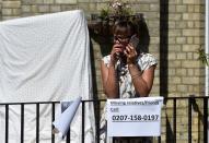 <p>A woman stands on a balcony behind a sign near a tower block severely damaged by a serious fire, in north Kensington, West London, Britain. June 14, 2017. (Photo: Hannah McKay/Reuters) </p>