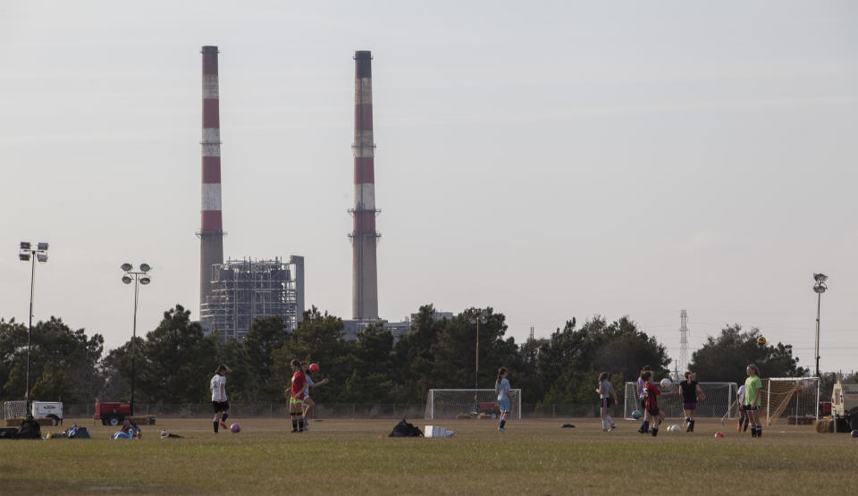 Girls play on a soccer fields near the L.V. Sutton Complex operated by Duke Energy in Wilmington, N.C., on Wednesday, Feb. 19, 2014. Members of the Flemington Road community near the plant, feel the facility could be polluting well water with spill off and seepage from large coal ash ponds. (AP Photo/Randall Hill)