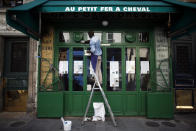 Cafe employee, Djibril, cleans the front window of a closed cafe, in Paris, Monday, June 1, 2020 as they prepare to reopen. Parisians who have been cooped up for months with take-out food and coffee will from Tuesday be able to savor their steak tartare in the fresh air and cobbled streets of the City of Light once more -- albeit in smaller numbers. (AP Photo/Thibault Camus)