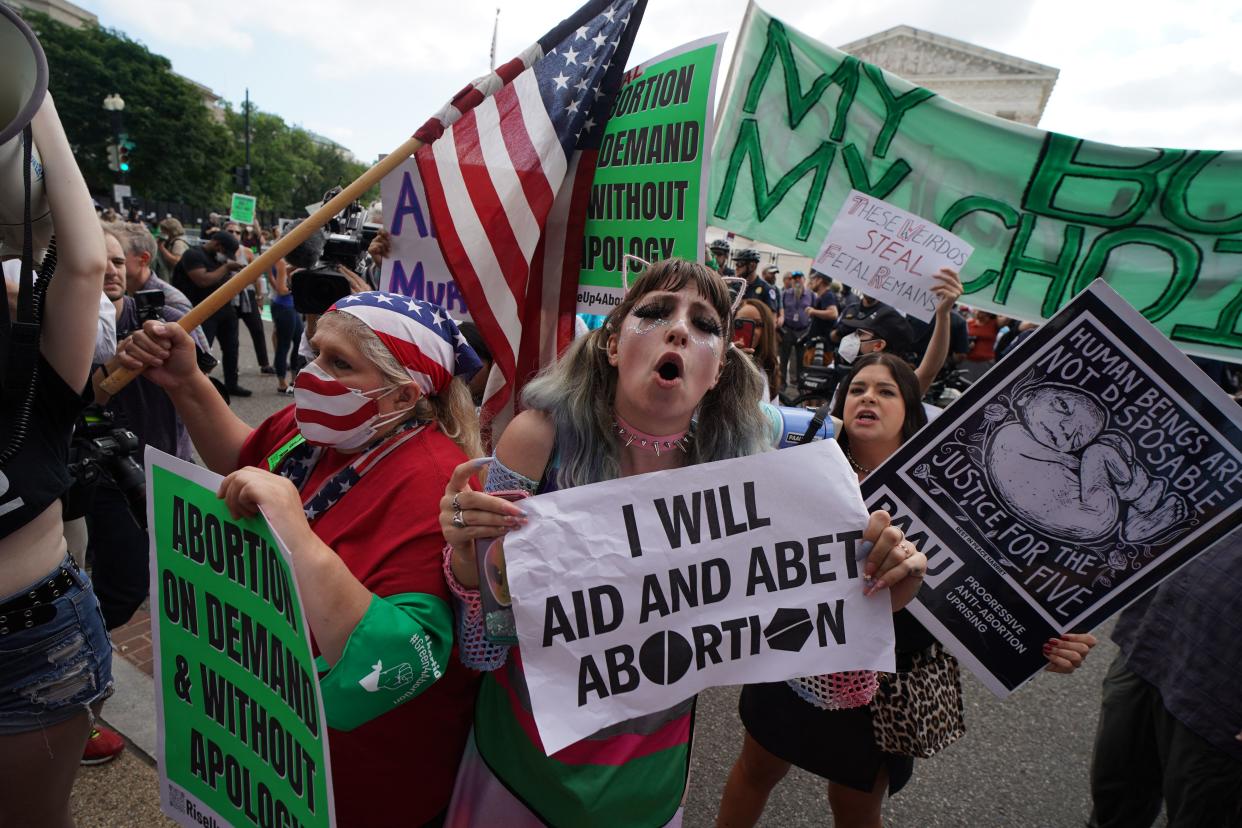 Pro-choice and anti-abortion demonstrators hold up signs reading: I will aid and abet abortion, and Human beings are not disposable.