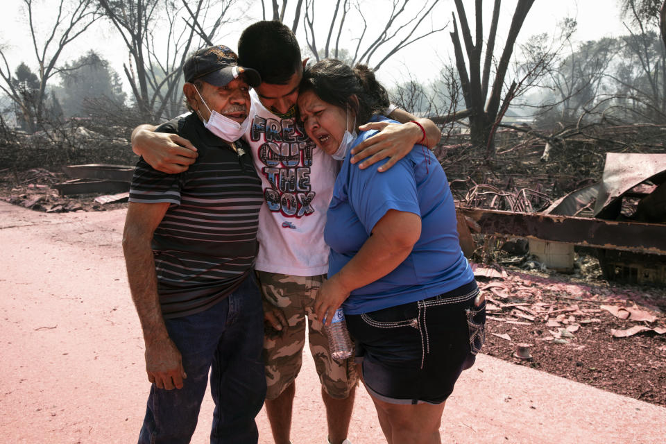 Dora Negrete, right, and her husband Marcelino Rocha, left, and son Hector Rocha console each other after seeing their destroyed mobile home at the Talent Mobile Estates as wild fires devastate the region on Thursday, Sept. 10, 2020 in Talent, Ore. (AP Photo/Paula Bronstein)