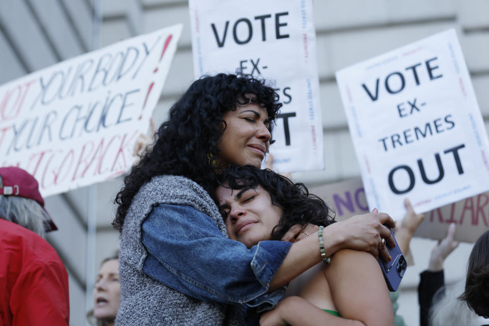 A woman hugs her daughter during an abortion rights protest. Demonstrators behind them hold signs reading: Vote extremes out.