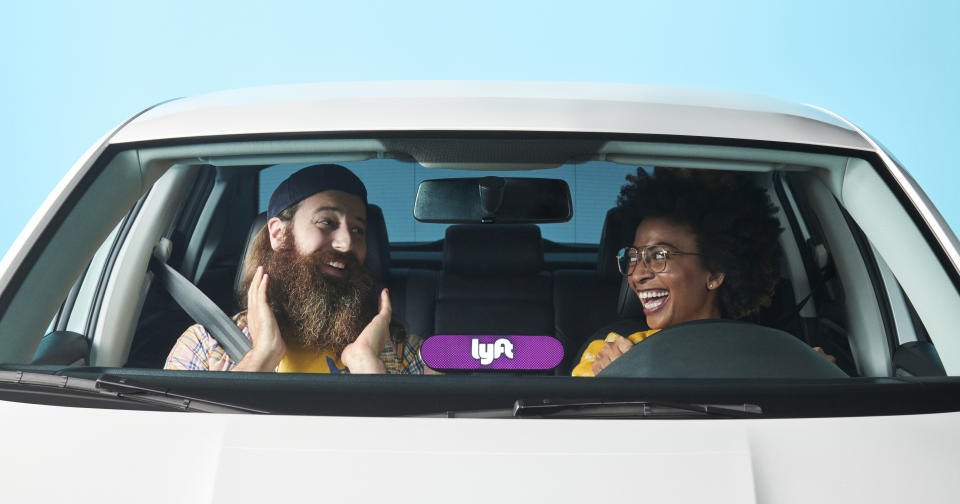 A smiling female Lyft driver in a car with a delighted bearded passenger.