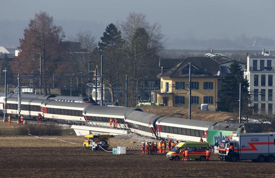 Rescue workers stand next to a derailed train after two trains collided near Rafz