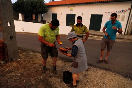 A woman gives cakes and beers to the villagers during a forest fire at the village of Colos