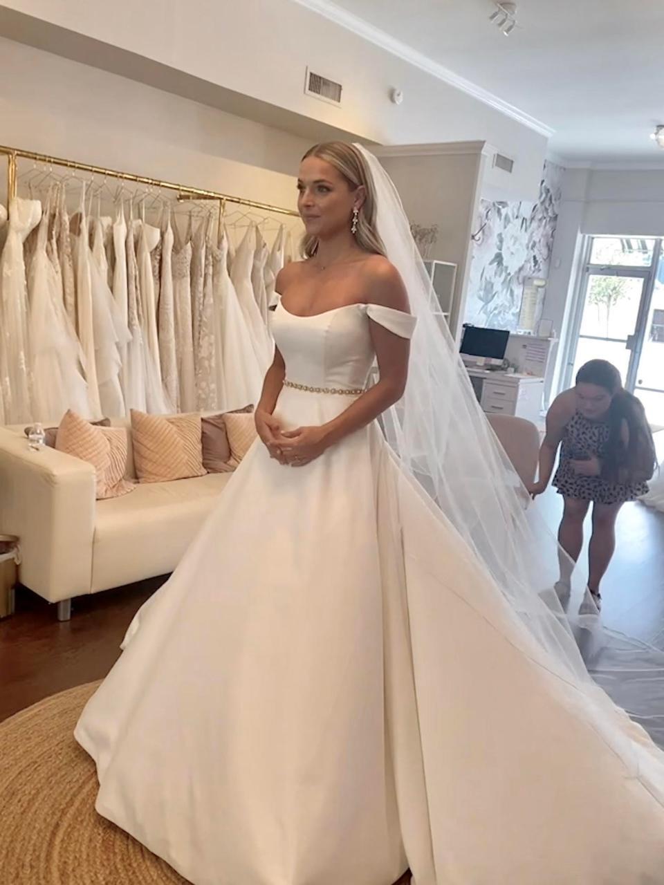 A bride stands in a wedding dress in a wedding boutique.