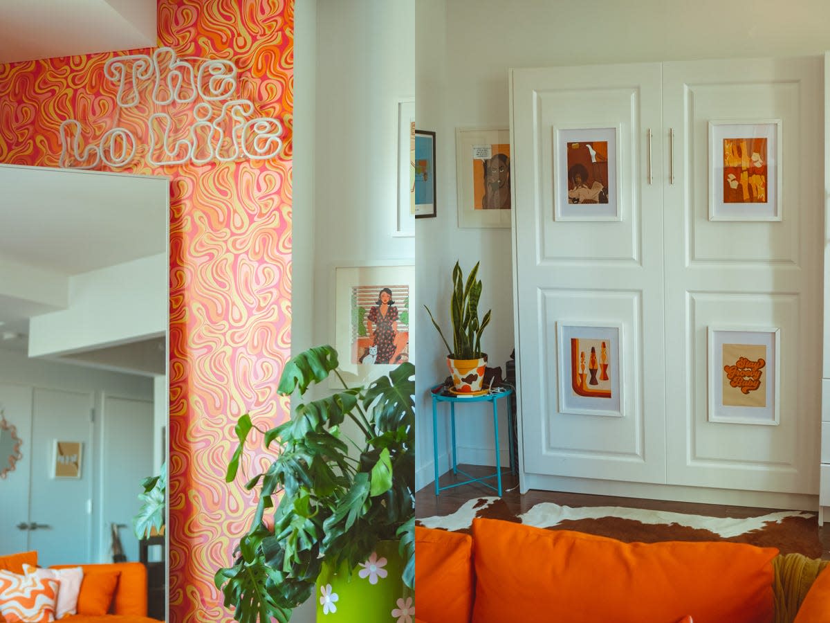 A wall with an orange and pink decal and "The Lo Life" neon sign on it; A folded up murphy bed with framed art on it and an orange couch in front