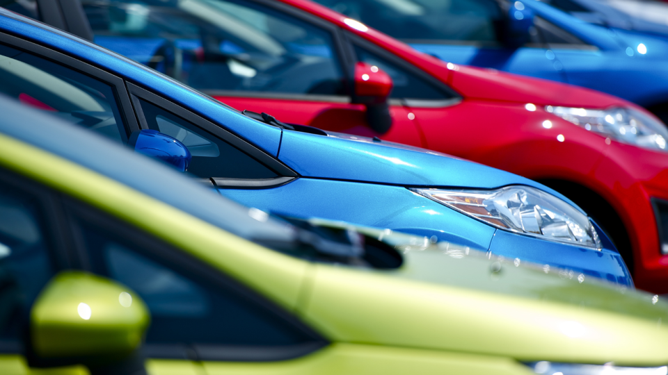 A row of cars of different colours in a car lot.