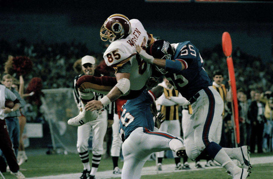Washington Redskins Don Warren (85) goes over New York Giants Gary Reasons (55) and Lawrence Taylor (56) to score a touchdown during action at RFK Stadium in Washington, Nov. 18, 1985. (AP Photo/J. Scott Applewhite)