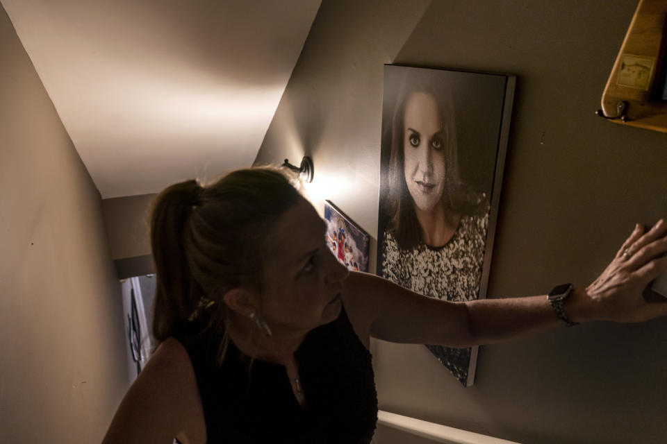 Janet Paulsen passes a photo of herself as she slowly climbs the staircase at her home in Acworth, Ga., Tuesday, Aug. 8, 2023. Paulsen was shot six times when her estranged husband ambushed her in their garage in 2015 before he turned the gun on himself. (AP Photo/David Goldman)