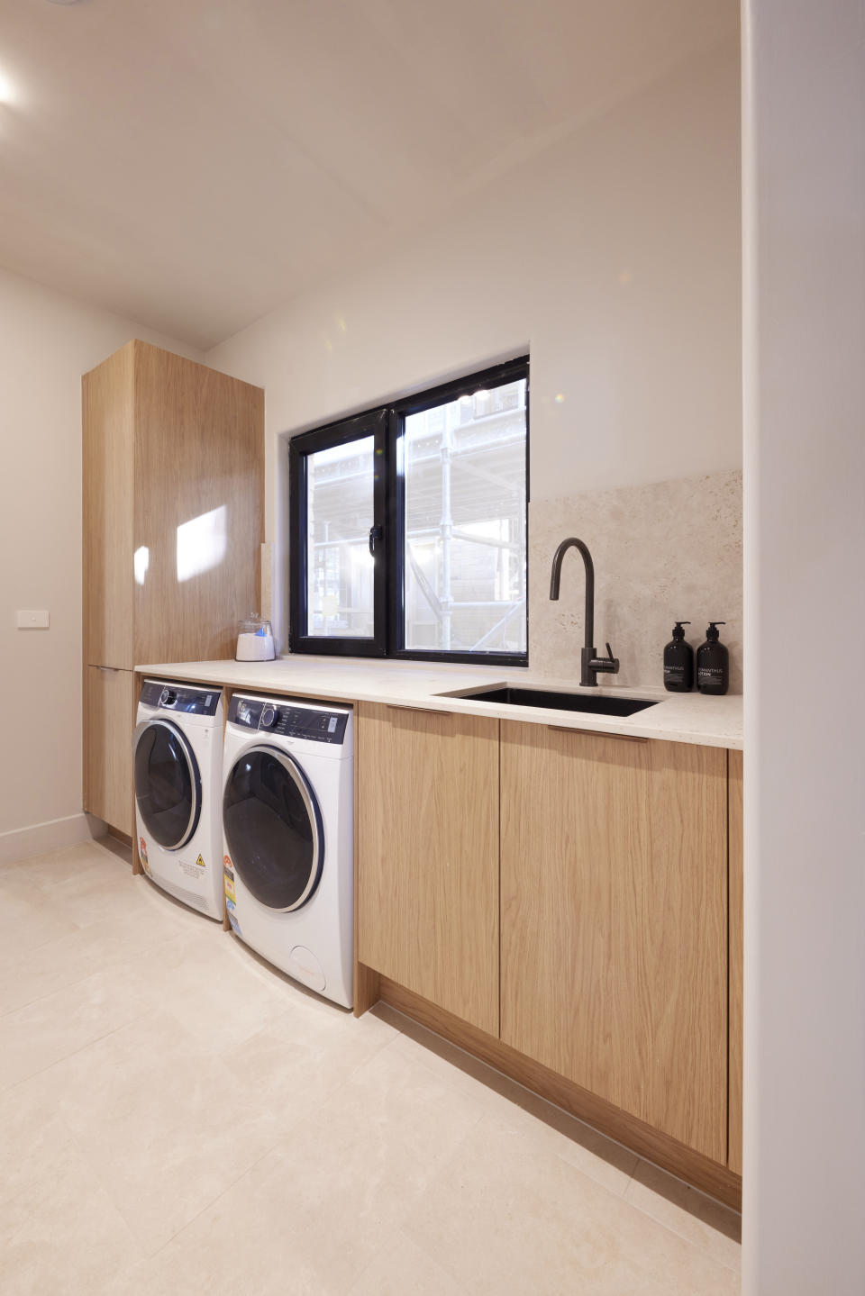 A wide shot of the laundry with a washer and dryer on the left, and light wooded cupboard and bench space above. 