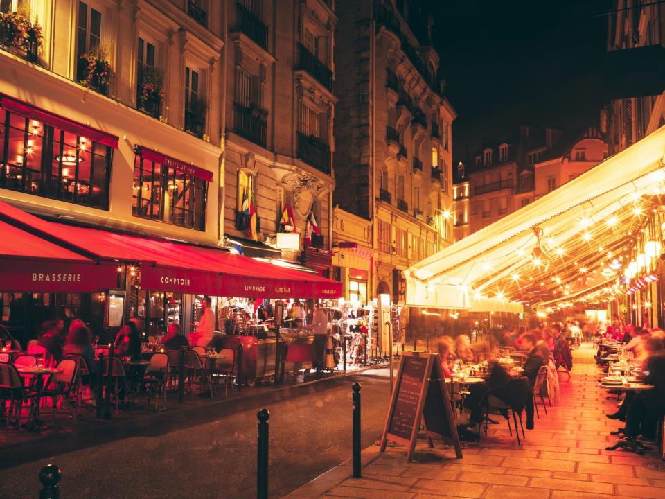 Paris street at nighttime with awnings of restaurants and diners seated outside