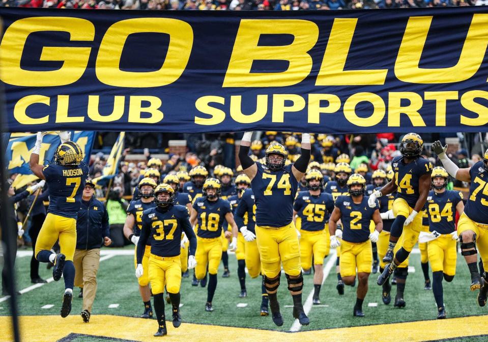 Michigan players jump up to touch the banner as they take the field for the Ohio State game at Michigan Stadium, Saturday, Nov. 30, 2019.