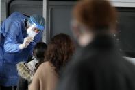 A member of the medical staff at the National Public Health Organisation (EODY) conducts a COVID-19 rapid test on a woman in Athens, Greece, Wednesday, Dec. 29, 2021. A government committee of medical experts hold an emergency meeting Wednesday to consider speeding up scheduled restrictions after the daily number of COVID-19 infections more than doubled in a day to set a new record. (AP Photo/Thanassis Stavrakis)