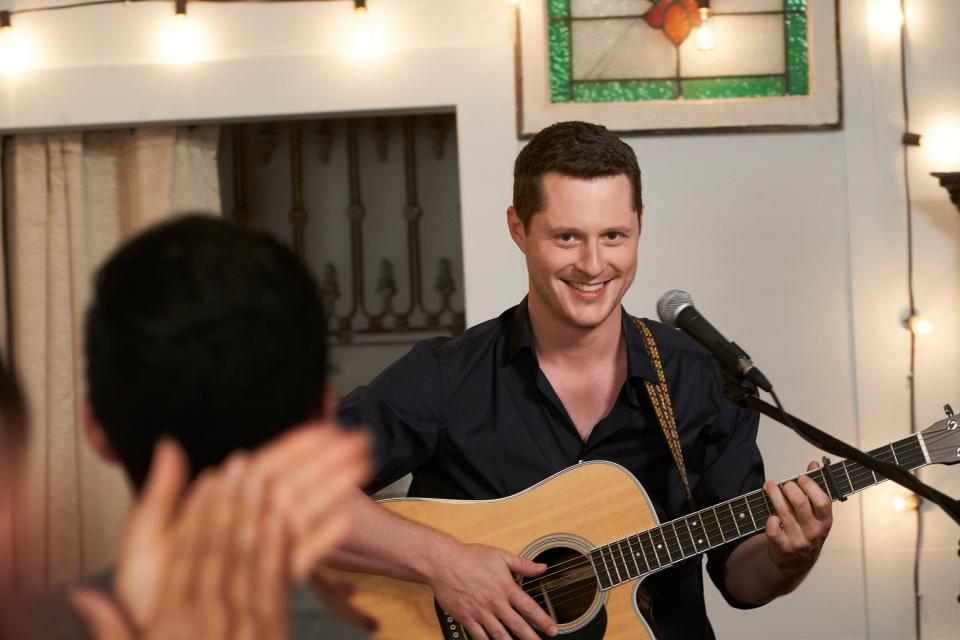 Noah Reid smiling while playing guitar.