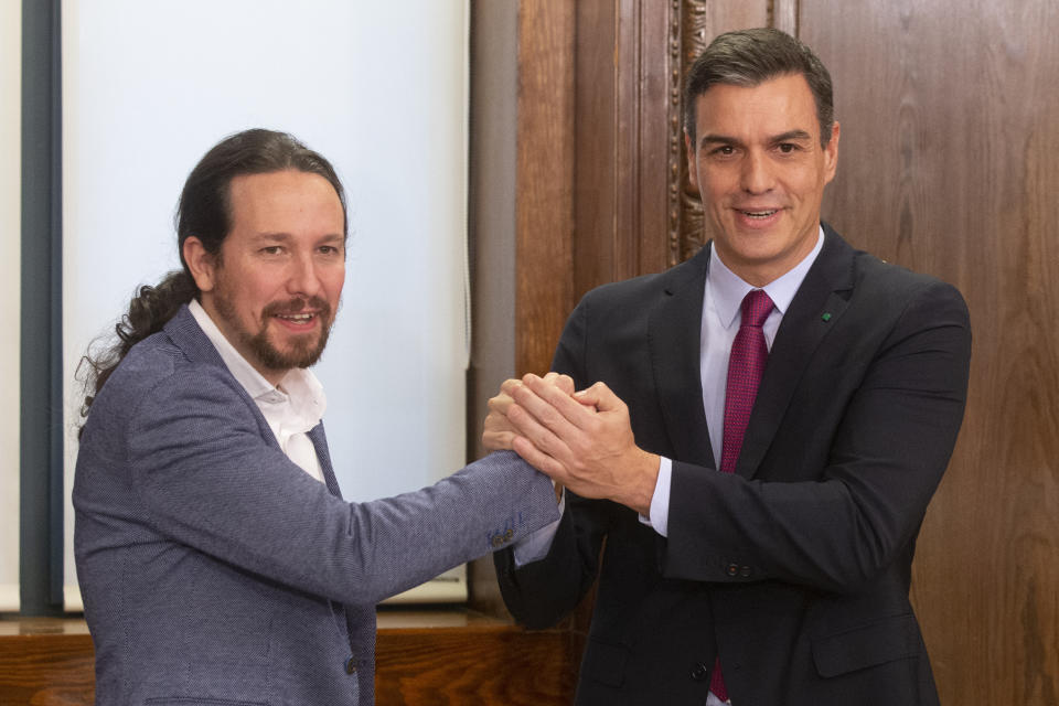 Spain's caretaker Prime Minister Pedro Sanchez, right and Podemos party leader Pablo Iglesias clasp hands after signing an agreement between the two parties in the Spanish parliament in Madrid, Spain, Monday, Dec. 30, 2019. Sanchez hopes to form center-left governing alliance to take office in the country in the coming days. (AP Photo/Paul White)