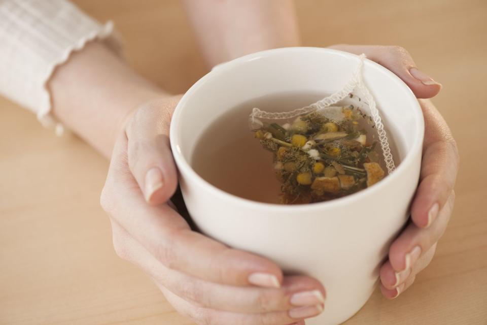feminine hands holding white mug of chamomile tea
