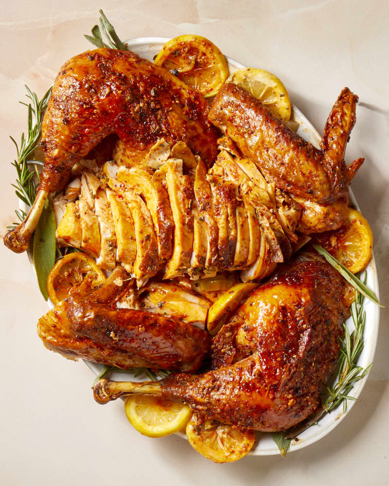 Overhead shot of a carved turkey resting on herbs and lemons on a white platter.