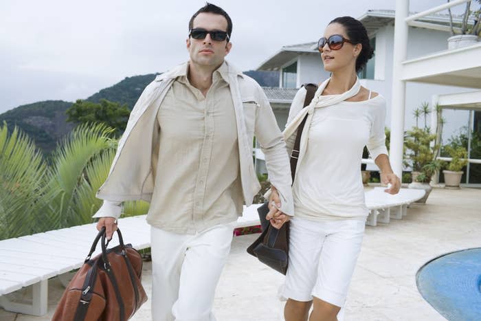 A wealthy couple walk hand-in-hand by a pool