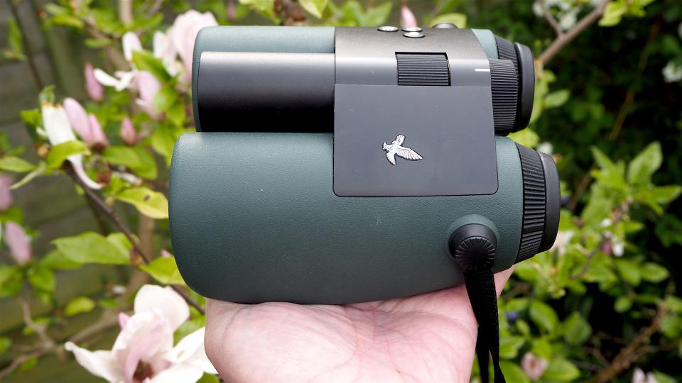 Swarovski Optik AX Visio binoculars held in a hand in front of a green bush