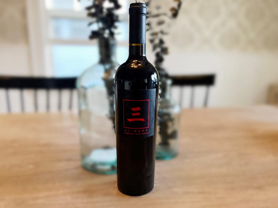 A bottle of Dwyane Wade's Three By Wade Cabernet Sauvignon sits on a table in front of a vase.