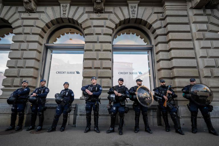 Agentes de la policía antidisturbios toman posición frente a la sede del banco Credit Suisse antes de una manifestación tras el anuncio de que el gigante bancario suizo UBS había acordado hacerse cargo de Credit Suisse en un acuerdo negociado por el gobierno en Zúrich, el 20 de marzo de 2023. (Fabrice COFFRINI / AFP)